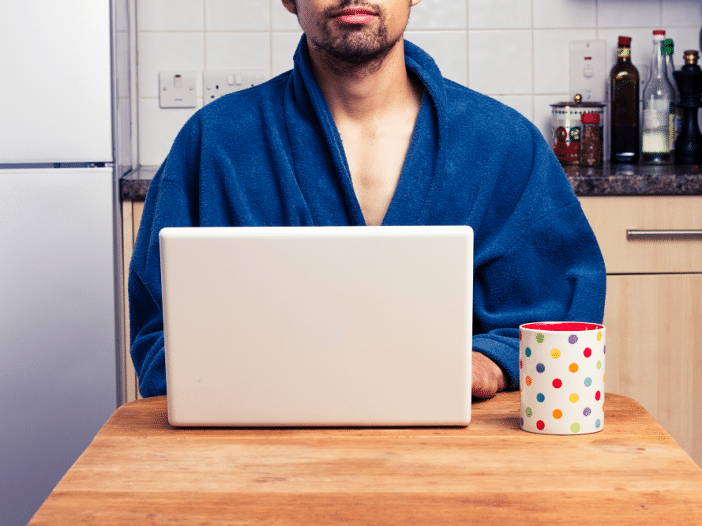 man wearing bathrobe works securely on a laptop at his dining room table at home