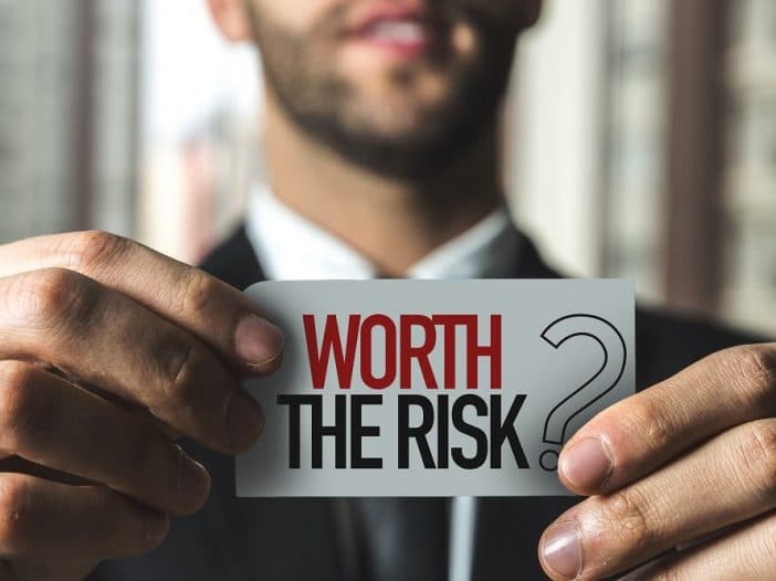 Man holding up a paper sign that says Is the risk worth it?