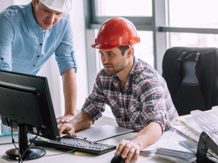 Two construction workers sitting at a computer